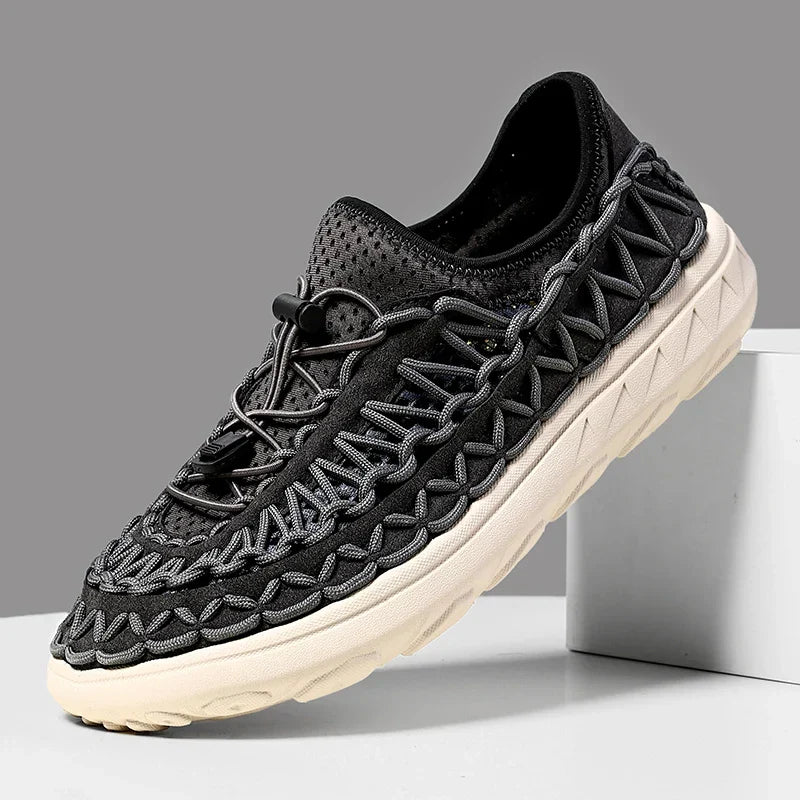 Black woven waterproof sneakers with rope-like lacing and a tan sole.