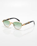 Gold-framed cat-eye sunglasses with green gradient lenses and black arms, detailed with gold accents, rest on a white surface.