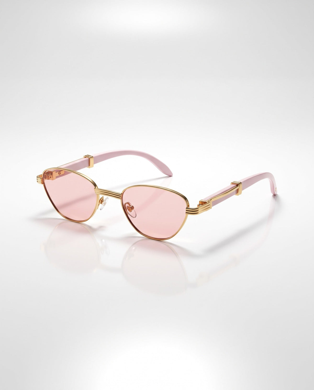 Gold cat-eye sunglasses with light pink lenses and matching pink arms featuring gold metal accents, on a reflective white surface.