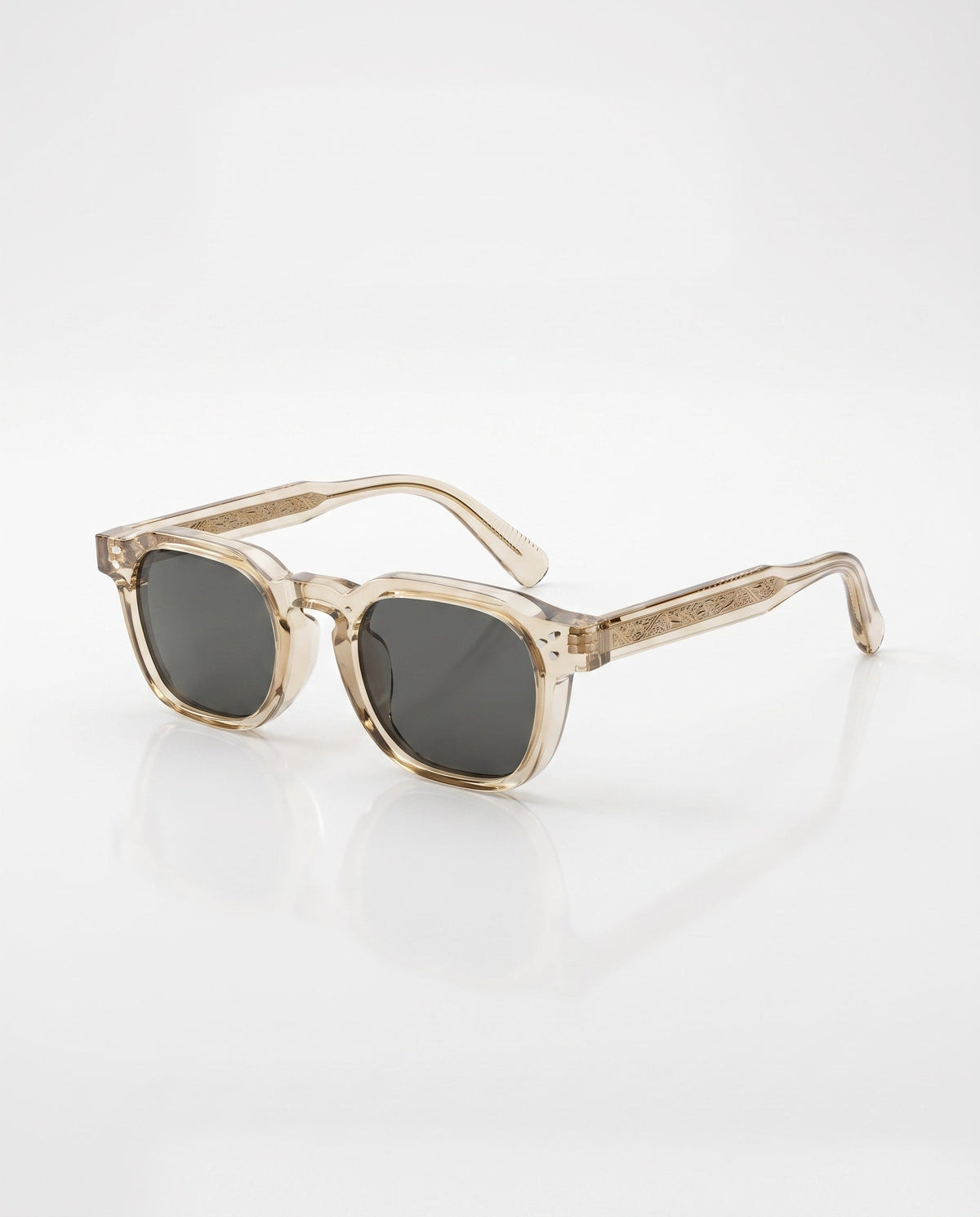 Translucent light brown square-framed sunglasses with dark grey lenses and intricate engraving on the temples, viewed at an angle on a white background.