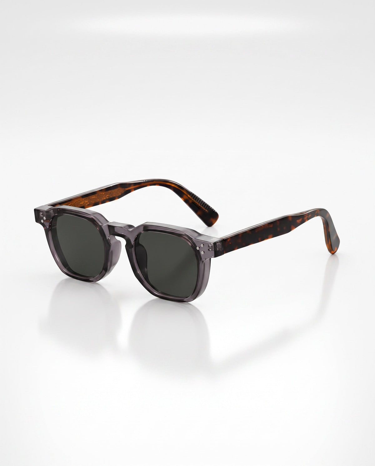 Translucent gray square-frame sunglasses with dark lenses and tortoiseshell arms sit angled on a reflective white surface.