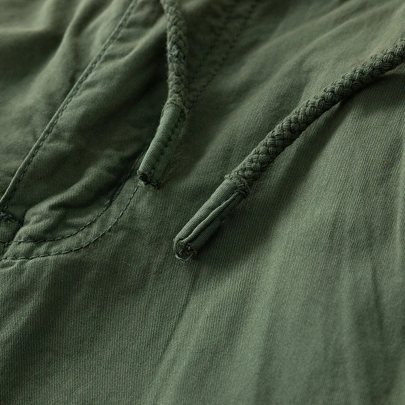Close-up of olive green cotton fabric with an adjustable braided drawstring and visible stitching details.