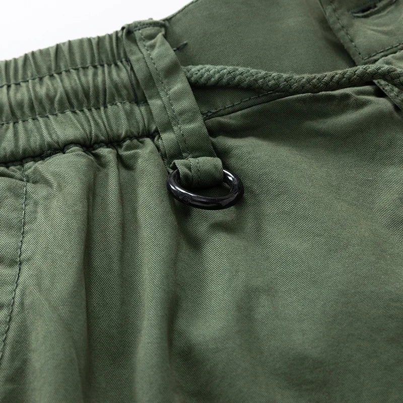 Close-up of olive green shorts showing an elasticated waistband, a black metal D-ring, and a matching drawstring.