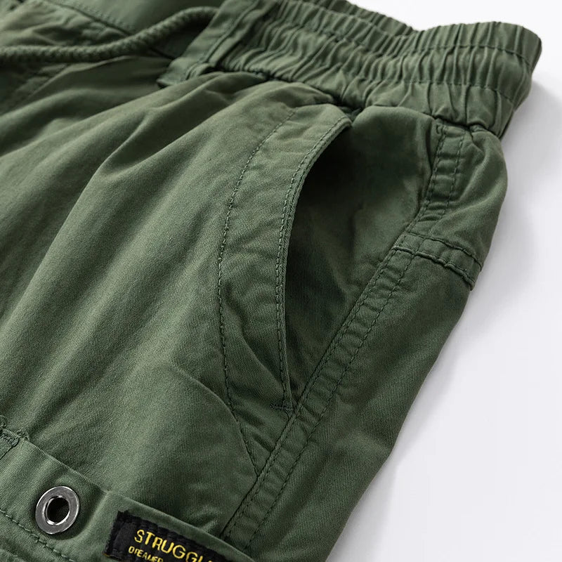 Close-up of olive green cotton shorts showing a ruched elastic waistband, a side pocket, and a drawstring detail.