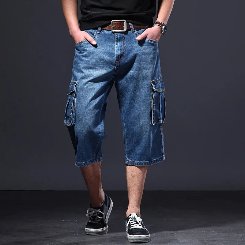 Man wearing distressed light blue denim cargo shorts with a brown belt and hands in pockets, standing against a dark background.
