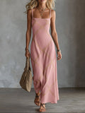 Woman wearing a pink spaghetti strap maxi dress with a gold diamond crisscross pattern, carrying a woven bag.