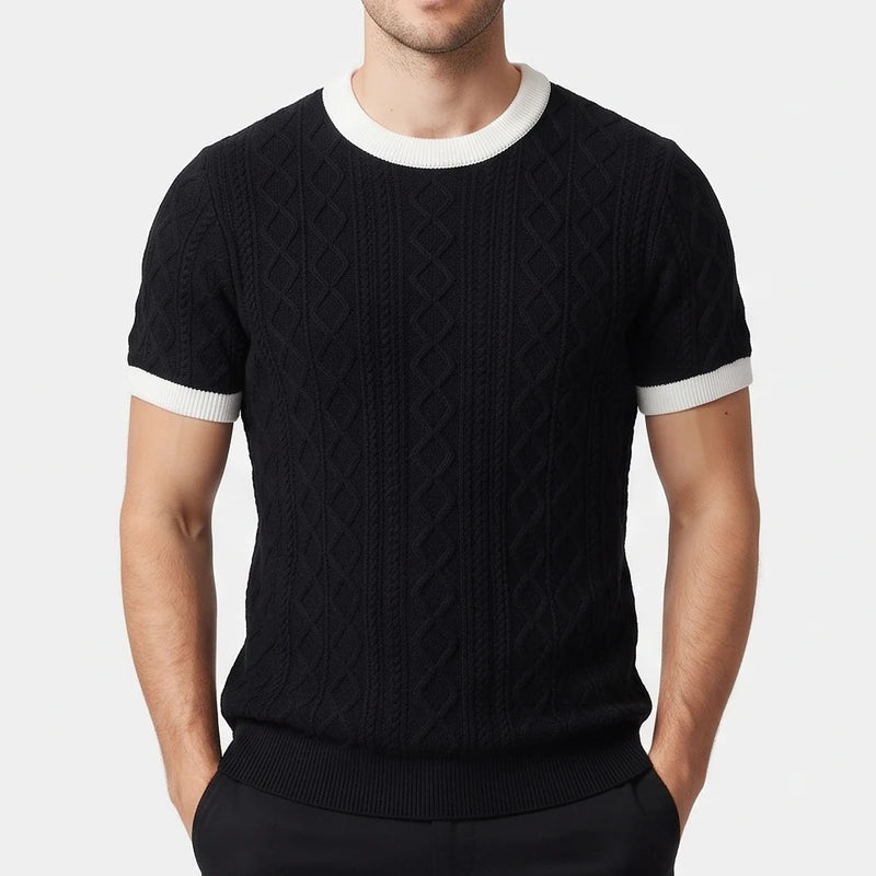 Man wearing a black short-sleeve cable knit shirt with white ribbed collar and cuffs, hands in pockets.