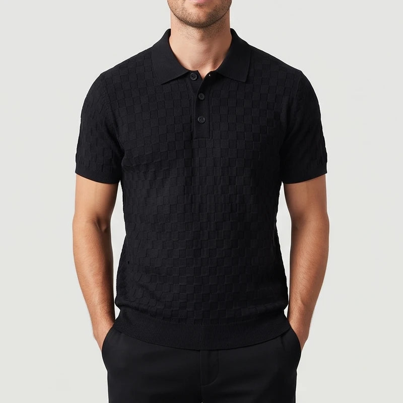 Man wearing a black short-sleeve knit polo shirt with a textured checkered pattern and three buttons, hands in pockets.