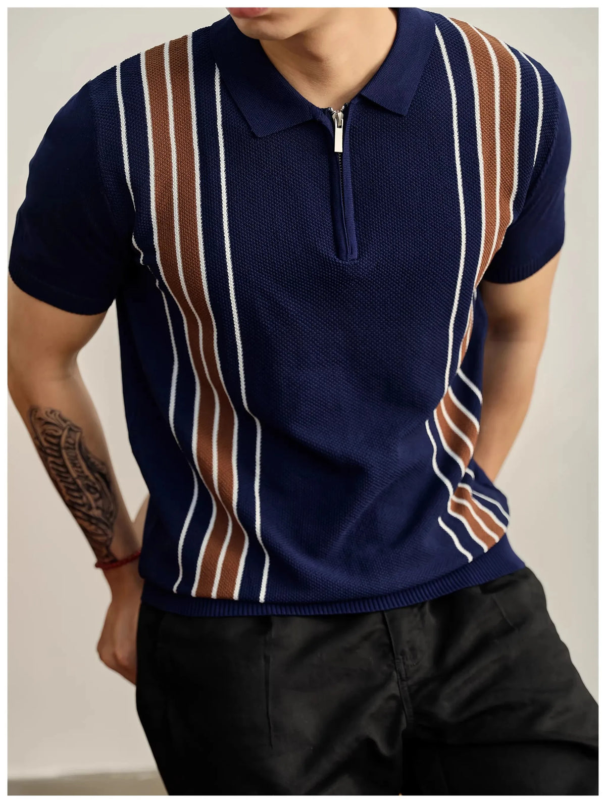 Man wearing a navy blue knit polo shirt with brown and white vertical stripes and a silver half-zip placket.