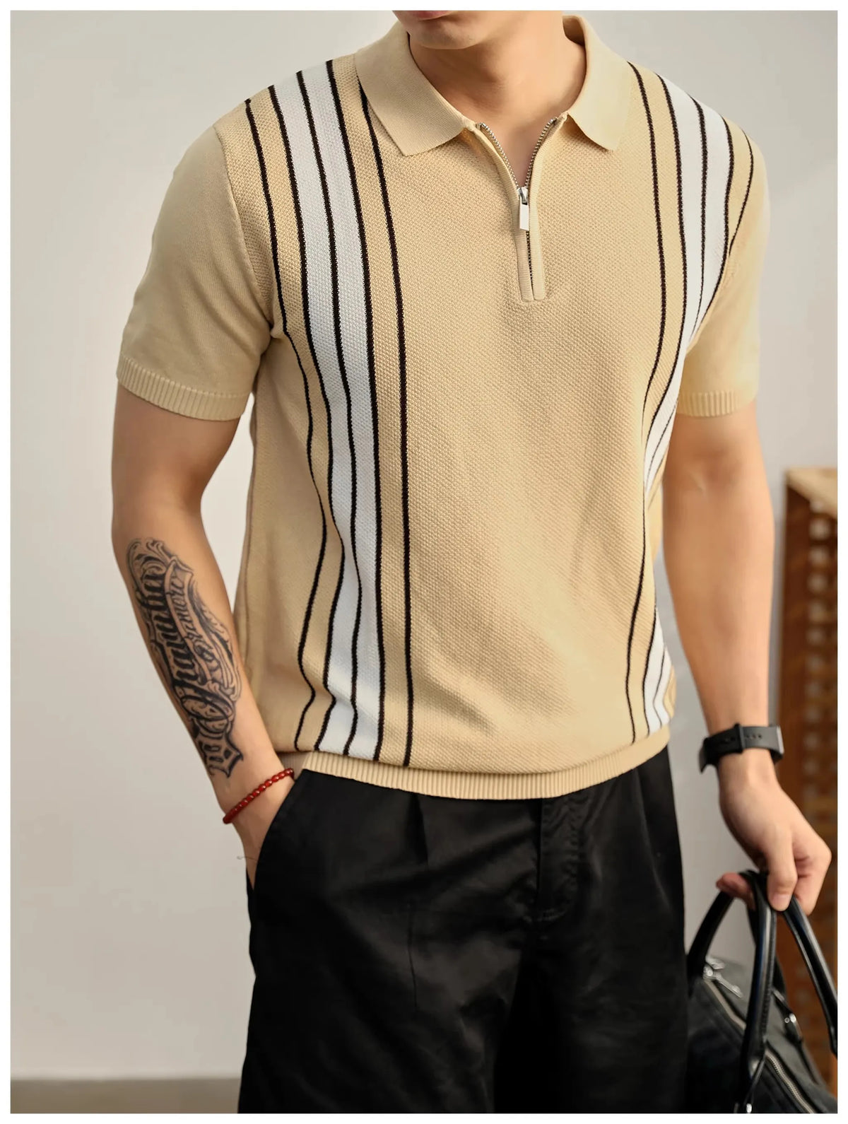 Man wearing a short-sleeved beige knit polo shirt with vertical white and black stripes, paired with black trousers.