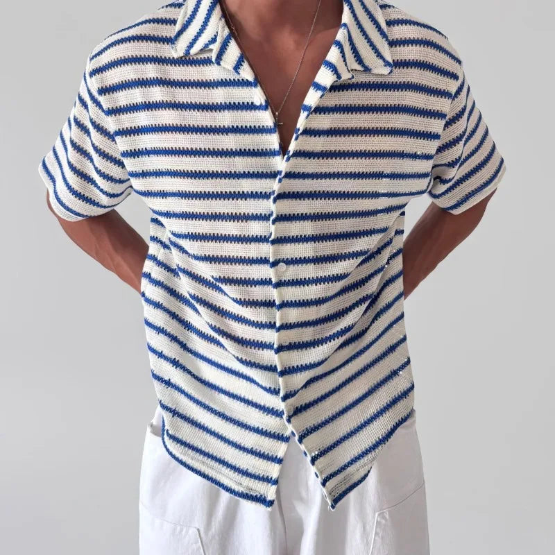 Man wearing a cream and blue striped open-knit shirt with short sleeves and white buttons, paired with white pants.