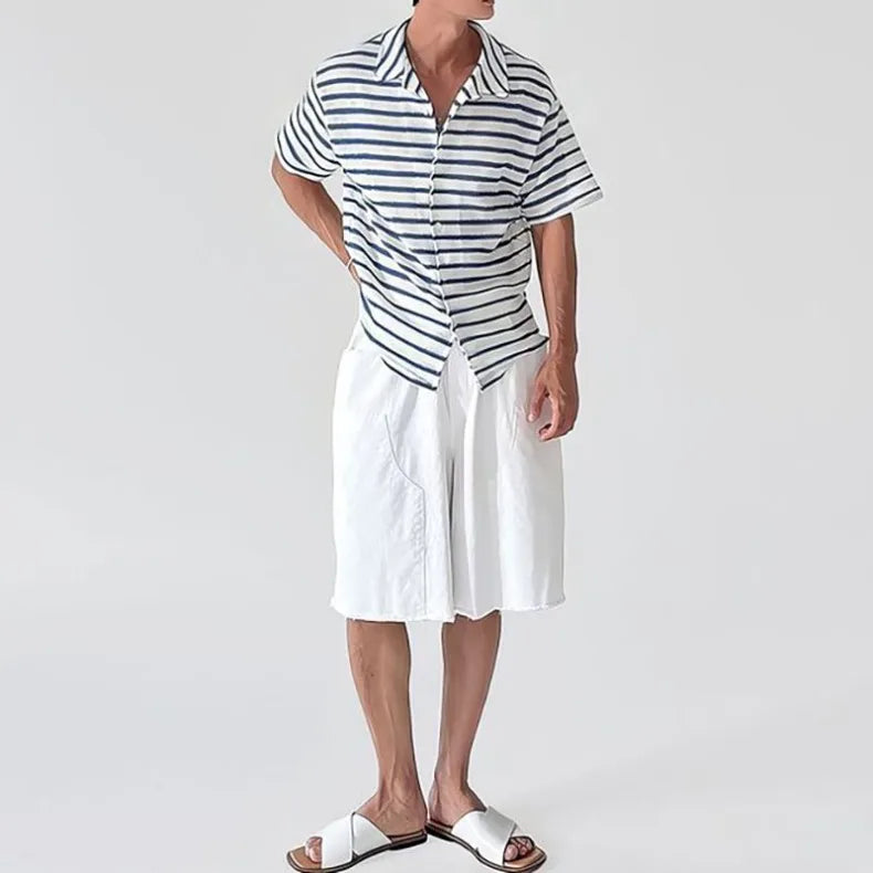 Man wearing a short-sleeved, open-collared knit shirt with white and navy blue horizontal stripes, paired with white shorts and sandals.