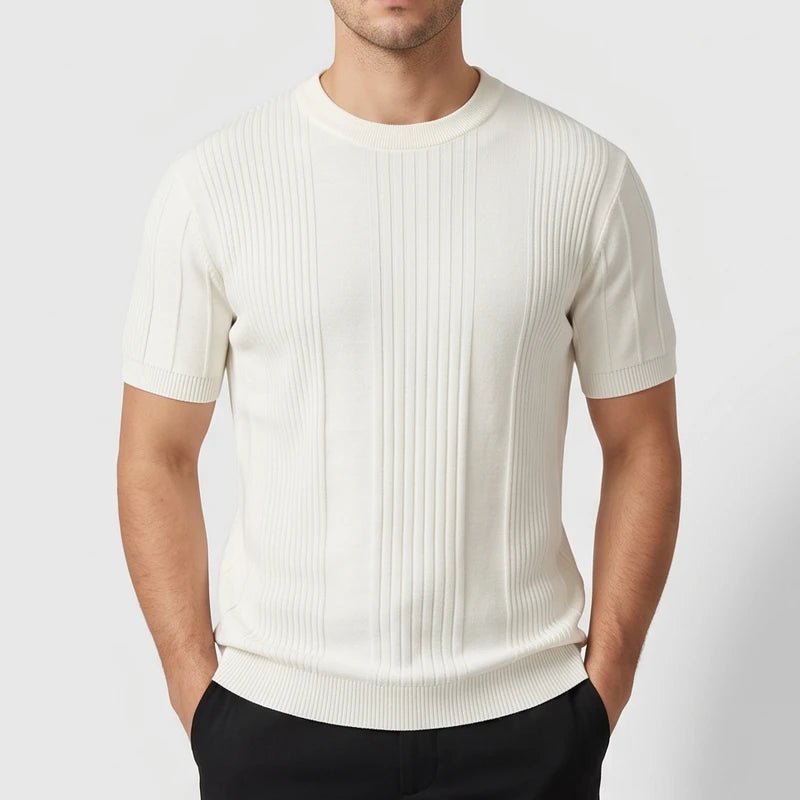Man wearing an off-white short-sleeve knit crewneck shirt with prominent vertical ribbing and fitted cuffs, hands in pockets.