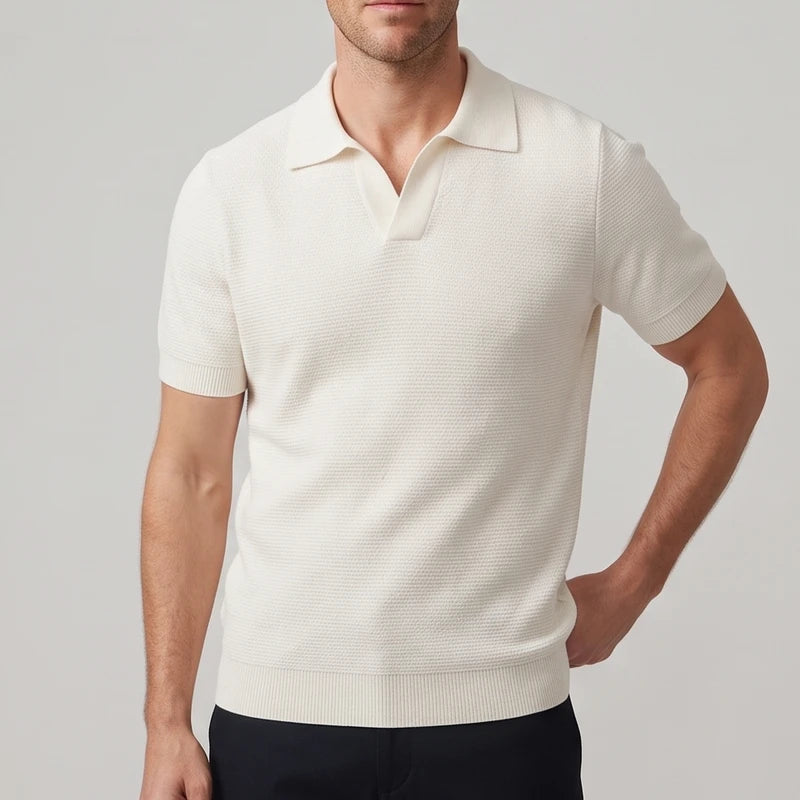 Man wearing a light cream textured knit short sleeve polo with a spread collar and open placket, hand in pocket.