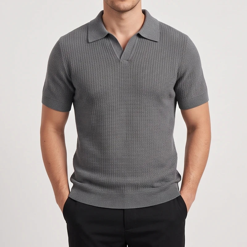 Man wearing a dark gray waffle knit short sleeve polo with an open notched collar, hands in black pants pockets.