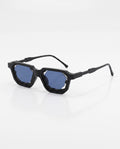 Angular black sunglasses with hexagonal blue lenses sit on a white background, angled slightly right.