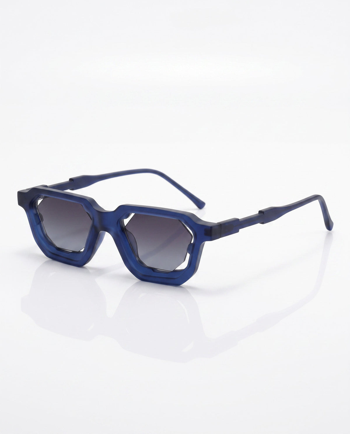 Matte blue angular sunglasses with dark gradient hexagonal lenses, shown at an angle on a white reflective surface.