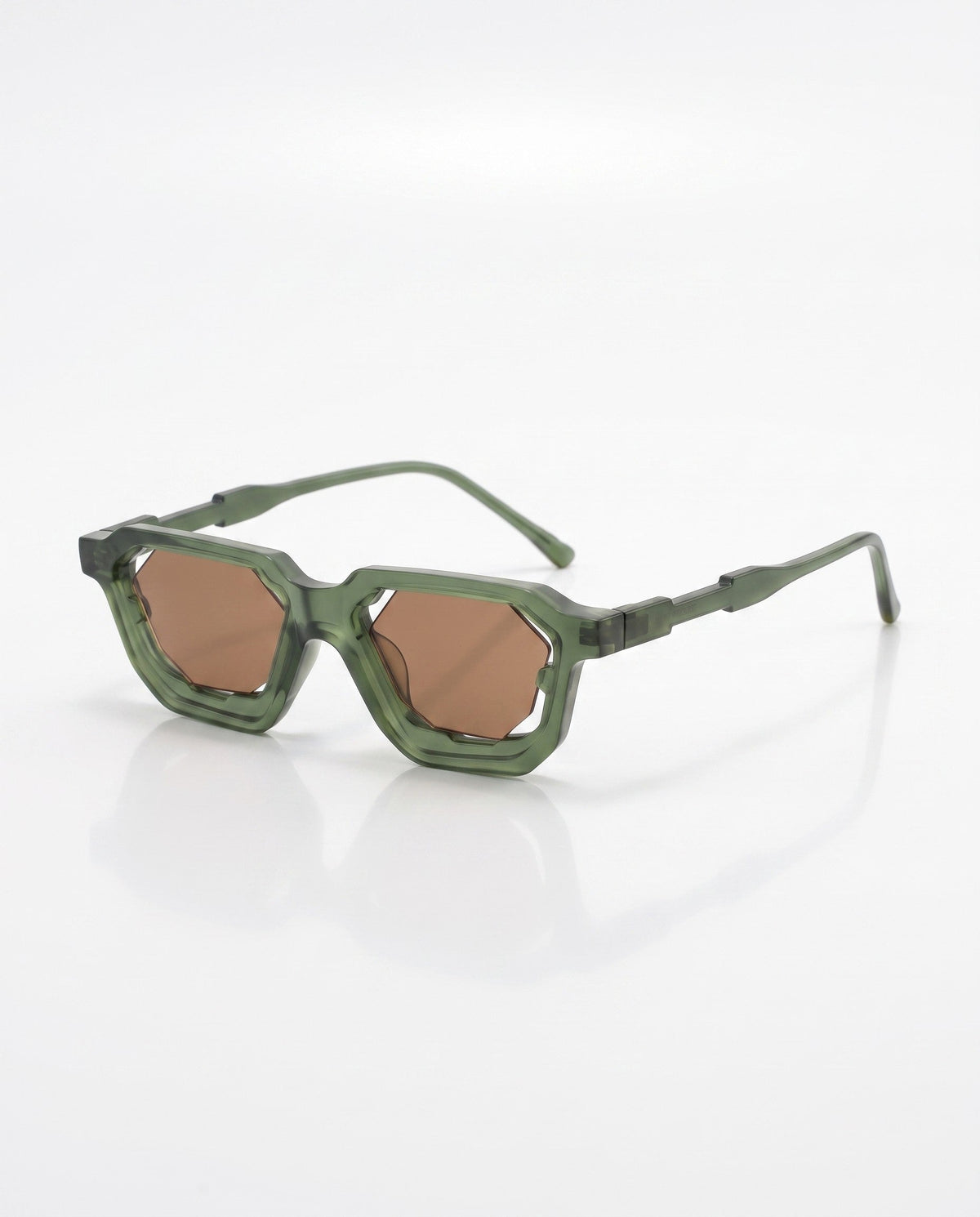 Green angular sunglasses with thick, translucent frames and geometric brown lenses lie on a white surface.