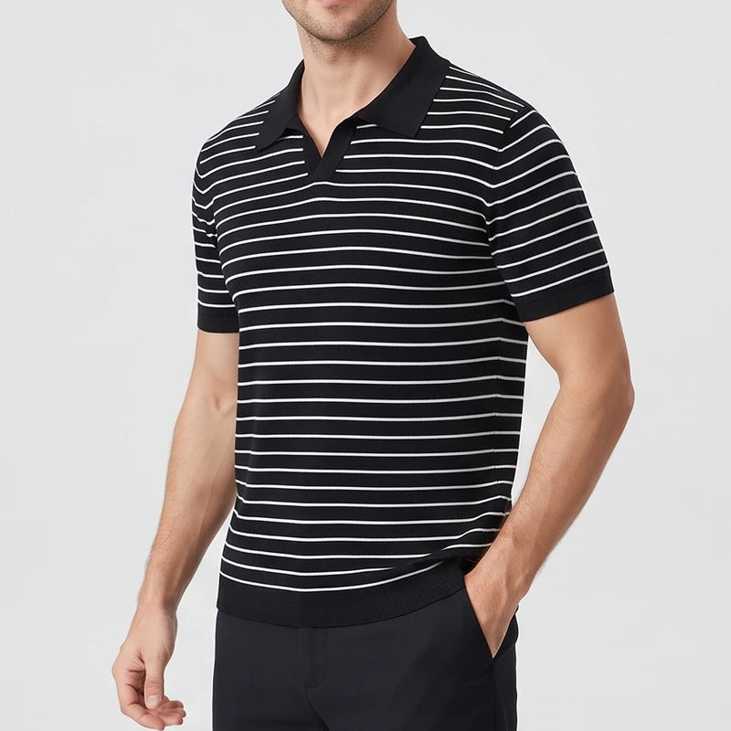 Man wearing a black and white striped short-sleeve polo shirt with a black collar, standing with a hand in his pocket.
