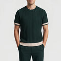 Man wearing a dark green short sleeve knit shirt with vertical cable knit texture and contrasting beige striped cuffs and hem.