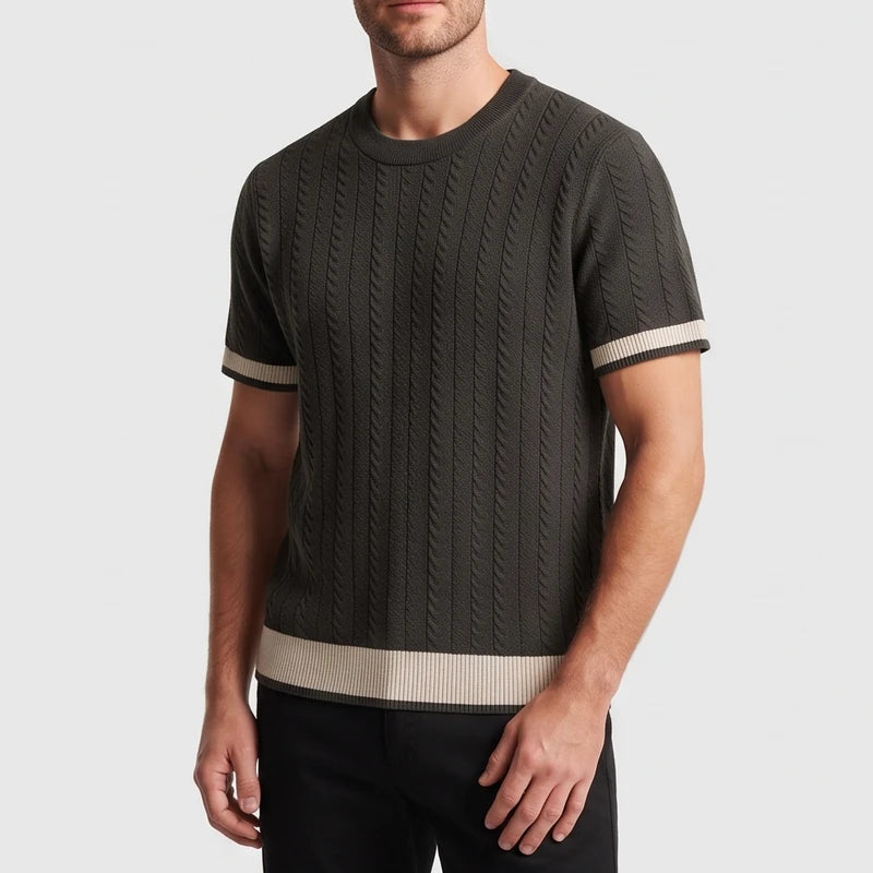 Man wearing a dark green cable knit short-sleeve shirt with beige striped cuffs and hem over black pants.