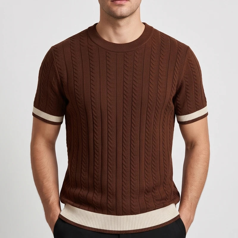 Man wearing a brown cable knit short sleeve shirt with beige stripes on the sleeves and hem, posing with hands in pockets.